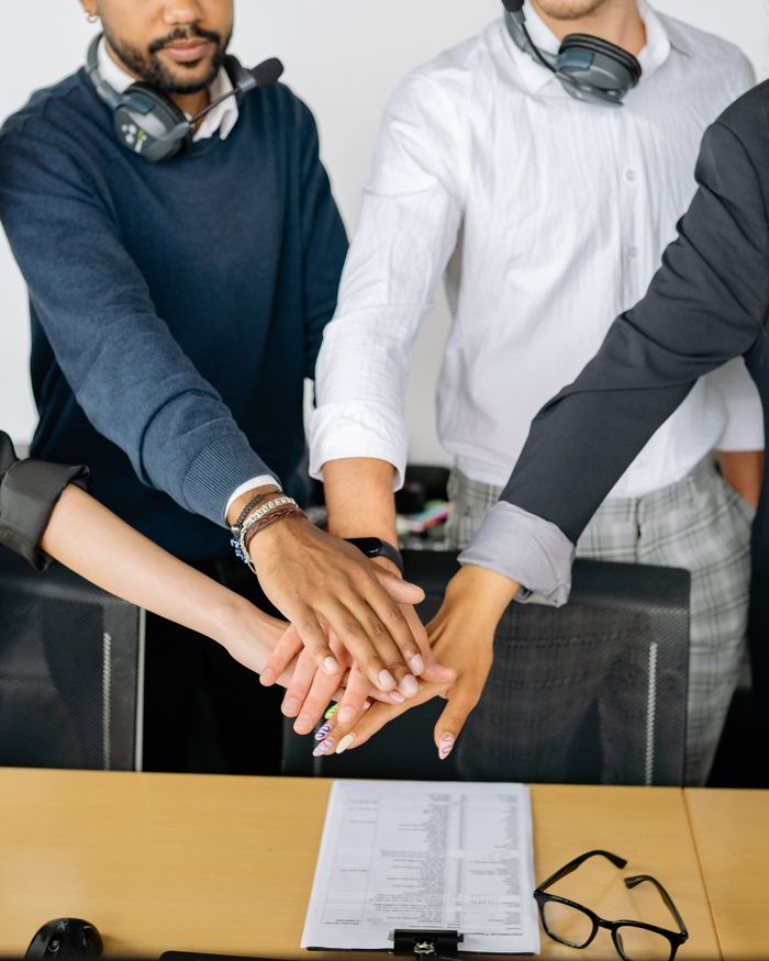 services-01 Diverse colleagues joining hands on conference table, symbolizing teamwork and unity.